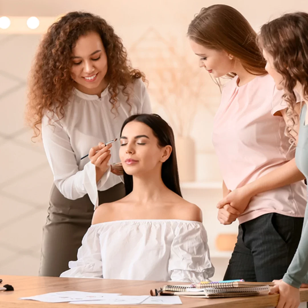 Makeup artist giving an on-demand makeup lesson to a client, demonstrating professional techniques while other students observe attentively.